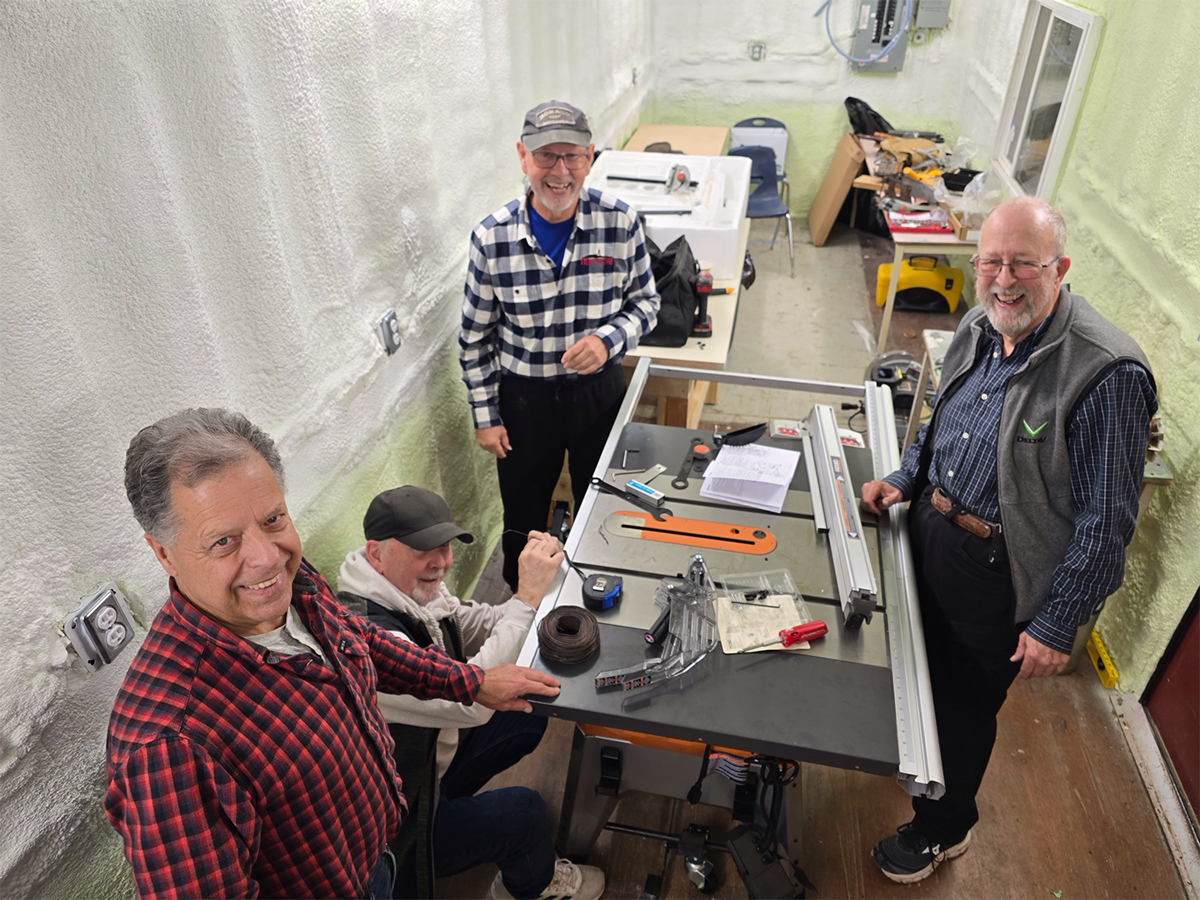 Four men work at a table saw inside an insulated sea-can workshop